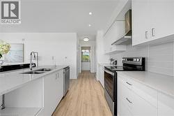 Kitchen featuring stainless steel appliances, white cabinets, light stone countertops, wall chimney range hood, and recessed lighting - 