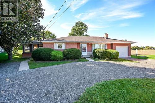 Red brick exterior with white window shutters, attached garage with white door, concrete walkway, and gravel driveway - 799 Highway 6, Caledonia, ON 