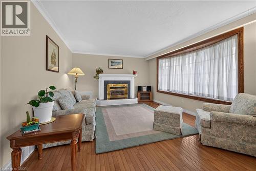 Hardwood flooring, crown molding, a decorative fireplace with a gold-toned insert, a bay window with wood trim, and neutral wall tones - 799 Highway 6, Caledonia, ON 