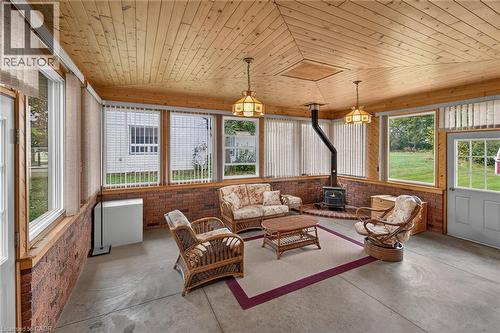 Wood-paneled ceiling, brick-finish wall accents, multiple windows, built-in wood-burning stove, and a light-colored entry door - 799 Highway 6, Caledonia, ON 