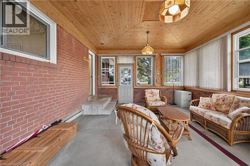 Enclosed sunroom featuring a vaulted wood-paneled ceiling, brick wall, multiple windows with vertical blinds, and a concrete floor - 799 Highway 6, Caledonia, ON 