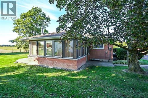 Brick exterior with a sunroom featuring multiple windows, a concrete patio, and a grass lawn with mature trees - 799 Highway 6, Caledonia, ON 