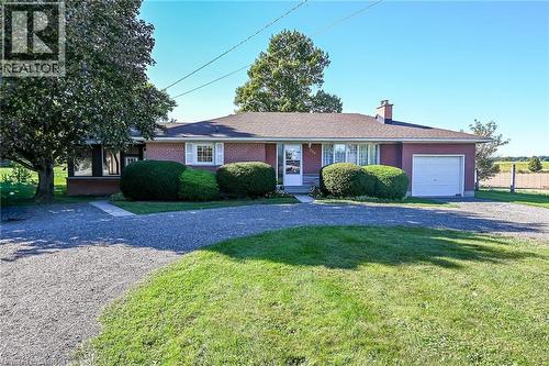 Brick exterior with a peaked shingle roof, attached garage, gravel driveway, and mature landscaping - 799 Highway 6, Caledonia, ON 