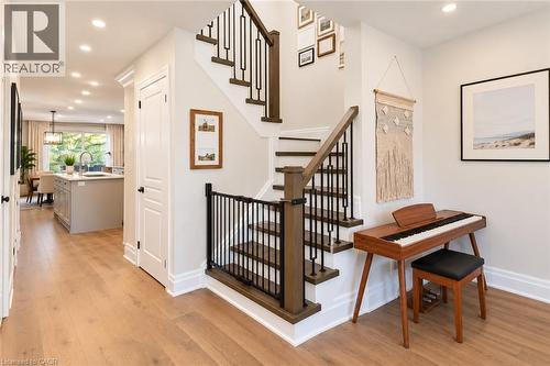 Light wood-finish flooring extending through the entry, staircase with dark wood-finish handrail and black metal balusters, recessed lighting, and white baseboards - 2409 Postmaster Drive, Oakville, ON 