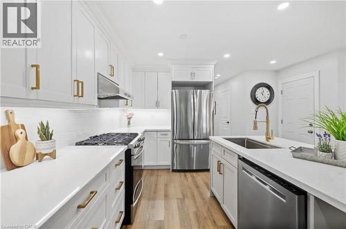 White cabinetry with gold-tone hardware, stainless steel appliances, wood-finish flooring, recessed lighting, and a kitchen island with an undermount sink - 2409 Postmaster Drive, Oakville, ON 