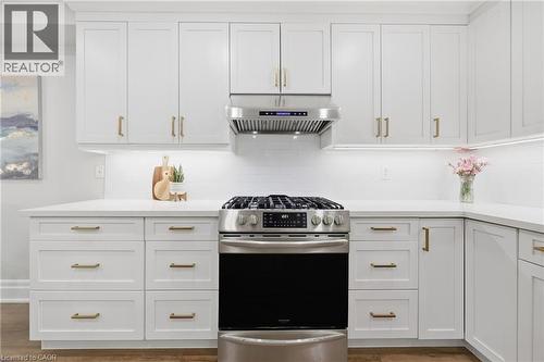 White shaker cabinetry with gold-tone hardware, stainless steel gas range, coordinating range hood, white subway tile backsplash, and light-toned countertops - 2409 Postmaster Drive, Oakville, ON 