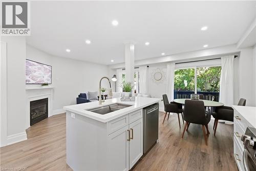 Open-concept living area with wood-finish flooring, a kitchen island with an undermount sink, a built-in fireplace with a mantel, and a sliding glass door to an exterior balcony - 2409 Postmaster Drive, Oakville, ON 