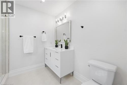 White vanity with integrated sink, matte black faucet, wall-mounted lighting fixture, framed mirror, and glass shower enclosure - 2409 Postmaster Drive, Oakville, ON 