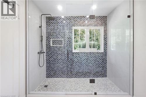 Glass-enclosed shower with pebble-finish flooring, a window, and a built-in shower niche - 2409 Postmaster Drive, Oakville, ON 