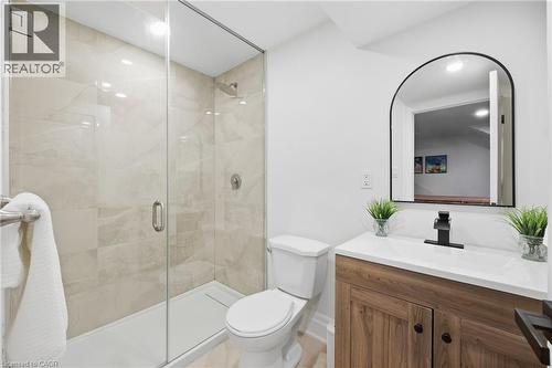 Walk-in shower with clear glass enclosure, a contemporary vanity with a wood-finish base, a white countertop with an integrated sink, and an arched mirror with a black frame - 2409 Postmaster Drive, Oakville, ON 
