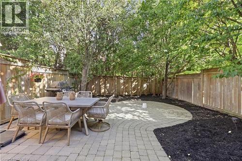 Private backyard featuring a paved patio, mature trees, wood fencing, and landscaped garden beds - 2409 Postmaster Drive, Oakville, ON 