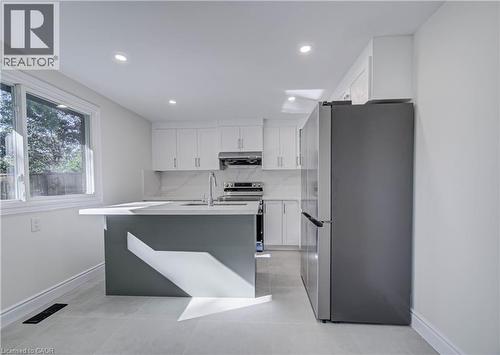 Kitchen featuring an island with a light-toned countertop, white cabinetry, a stainless steel refrigerator, and tiled flooring - 210 Ferguson Avenue, Cambridge, ON 