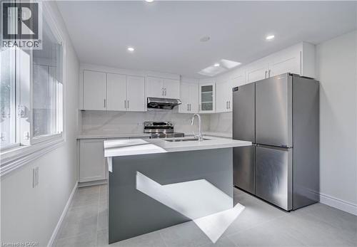 White shaker cabinetry, stainless steel appliances, central island with sink, recessed ceiling lighting, and light-toned flooring - 210 Ferguson Avenue, Cambridge, ON 