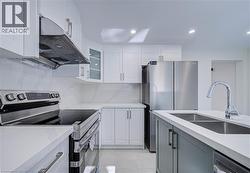 White shaker cabinetry, stainless steel appliances, white countertops, kitchen island with undermount double-basin sink, and recessed lighting - 