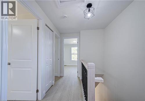 Hallway featuring wood-finish flooring, white paneled doors, a geometric light fixture, and a wood and metal railing - 210 Ferguson Avenue, Cambridge, ON 
