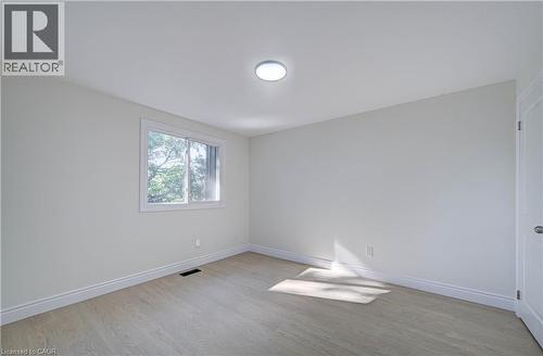 Light-colored wood-finish flooring, white walls, white trim, a single window, and a flush-mount ceiling light fixture - 210 Ferguson Avenue, Cambridge, ON 