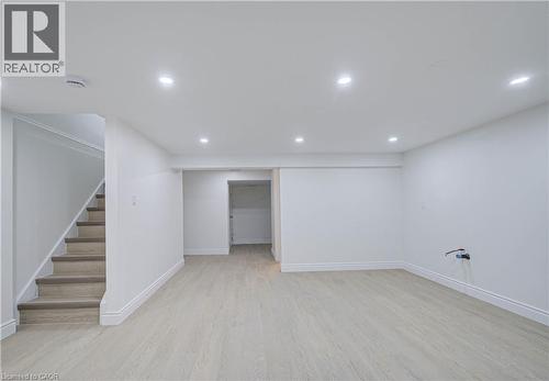 Spacious room featuring light-toned wood-finish flooring, recessed lighting, white walls, and a stairway with carpeted treads - 210 Ferguson Avenue, Cambridge, ON 