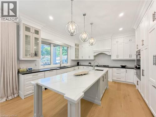 Gourmet kitchen featuring a large central island with light-toned countertops, extensive white cabinetry, wood-finish flooring, recessed lighting, and modern pendant fixtures - 236 Poplar Drive, Burlington, ON 