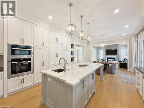 Bright kitchen featuring white cabinetry, integrated stainless steel appliances, a center island with a sink and stone countertop, and wood-finish flooring - 236 Poplar Drive, Burlington, ON 