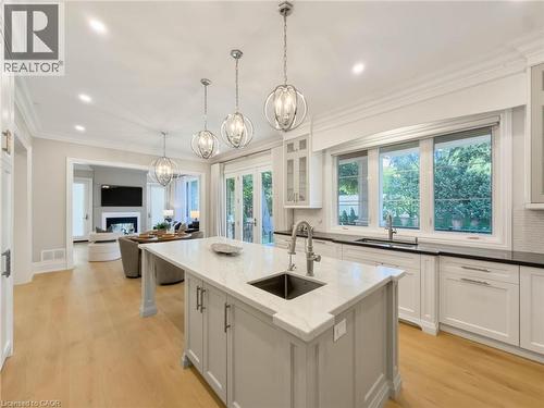 Kitchen featuring a central island with an undermount sink, pendant lighting, white cabinetry, and wood-finish flooring - 236 Poplar Drive, Burlington, ON 