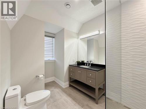 Built-in vanity with dark countertop, large vanity mirror with integrated lighting, and textured wall tile in the shower enclosure - 236 Poplar Drive, Burlington, ON 
