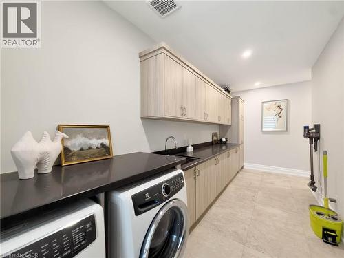 Integrated laundry appliances with dark countertops, a built-in sink, extensive upper and lower cabinetry, recessed lighting, and tile flooring - 236 Poplar Drive, Burlington, ON 