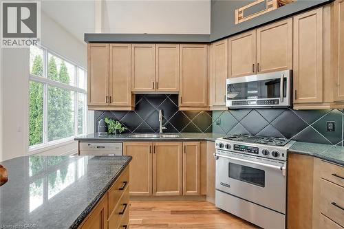 Wood-finish cabinetry complemented by dark countertops, stainless steel appliances, and a diagonal tile backsplash - 4285 Couples Crescent, Burlington, ON 
