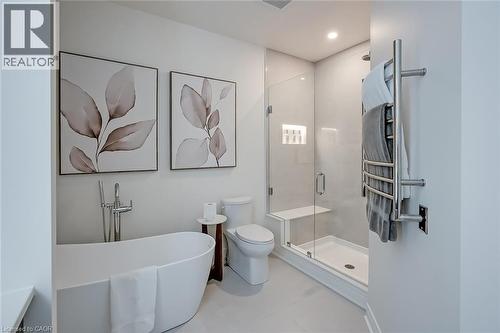Freestanding soaking tub with floor-mounted faucet, glass-enclosed shower with built-in bench and recessed shelving, and a wall-mounted towel warmer - 4285 Couples Crescent, Burlington, ON 