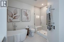 Freestanding soaking tub with floor-mounted faucet, glass-enclosed shower with built-in bench and recessed shelving, and a wall-mounted towel warmer - 