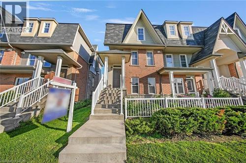 Brick facade townhome featuring a covered front porch, white railing, concrete steps, and dormer windows - 1380 Costigan Road Unit# 13, Milton, ON 