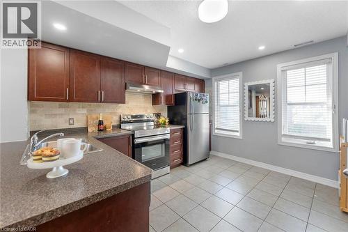 Kitchen featuring wood-finish cabinetry, stainless steel appliances, speckled countertops, and a subway tile backsplash - 1380 Costigan Road Unit# 13, Milton, ON 