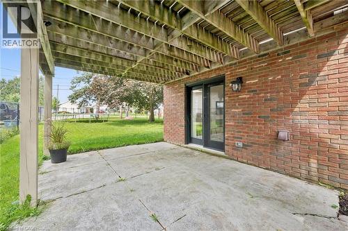 Concrete patio with overhead wood-beam deck structure and brick exterior wall - 8 Christian Street, Baden, ON 