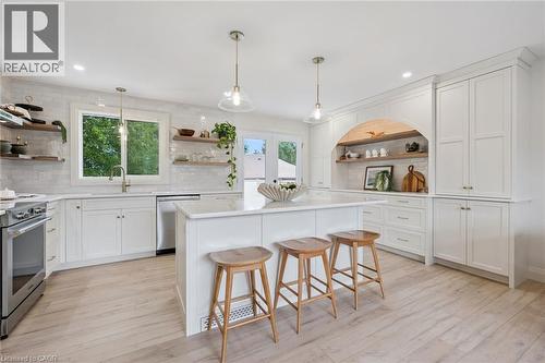 Kitchen featuring white cabinetry, wood-finish flooring, a central island with countertop, stainless steel appliances, and open shelving - 8 Christian Street, Baden, ON 