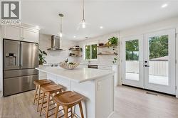 Kitchen featuring a center island with a light-toned countertop, stainless steel appliances, a tile backsplash, wood-finish flooring, and double glass-paned doors - 