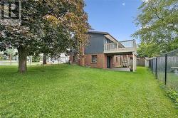 Expansive green space featuring mature trees, a multi-level wood deck, a chain-link fence, and a brick and siding exterior - 