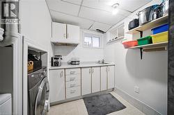 Dedicated laundry room featuring front-load washer, ample cabinetry with multiple drawers, stainless steel countertop, open shelving with organized storage bins, and practical layout designed for effi - 