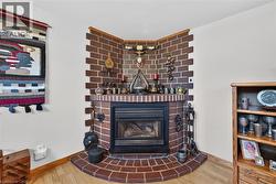 Corner gas fireplace featuring a masonry surround, brick hearth, and wood-finish flooring - 