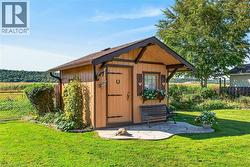 Outbuilding featuring vertical wood-finish siding, an overhanging gable roof with exposed decorative brackets, a single door with iron-style hardware, and an irregular stone patio - 