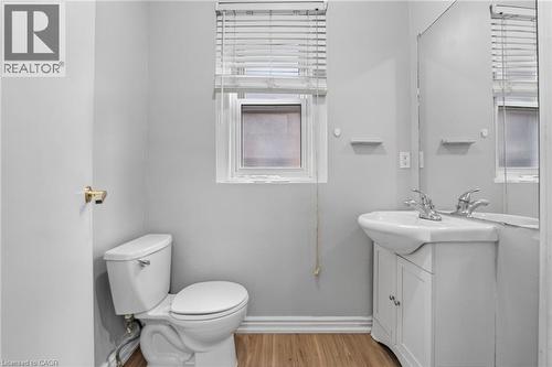 Wood-finish flooring, single window with blinds, white toilet, vanity with integrated basin, wall-mounted mirror - 199 N Locke Street N, Hamilton, ON 