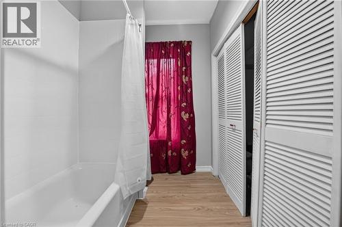 White tub with shower surround, wood-finish flooring, and white louvered bifold doors - 199 N Locke Street N, Hamilton, ON 