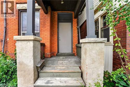 Brick exterior with stone window sills, wood-frame windows, and a covered porch featuring stone pillars and painted wood steps - 199 N Locke Street N, Hamilton, ON 