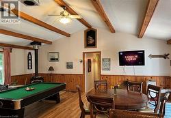 Vaulted ceiling with exposed wood beams, wood-finish flooring, wood-paneled wainscoting, and a freestanding wood-burning stove - 