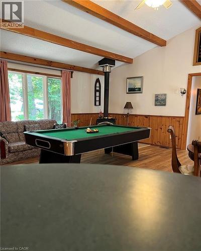Vaulted ceiling with exposed wood beams, wood-finish flooring, wood paneling, and a built-in wood stove - 16431 Highway 35, Algonquin Highlands, ON 