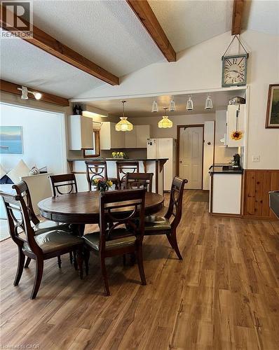 Wood-finish flooring, exposed ceiling beams, white vaulted ceiling, white kitchen cabinetry, and a kitchen island with dark countertops - 16431 Highway 35, Algonquin Highlands, ON 