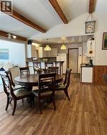 Wood-finish flooring, exposed ceiling beams, white vaulted ceiling, white kitchen cabinetry, and a kitchen island with dark countertops - 