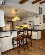 Kitchen featuring white cabinetry, dark countertops, wood-finish flooring, and a breakfast bar with built-in storage - 