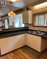 Kitchen featuring wood-finish flooring, white cabinetry with wood trim, dark countertops, and a double basin stainless steel sink - 