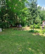 Expansive lawn area with a central fire pit structure and surrounding stone seating, bordered by mature trees and natural landscaping - 