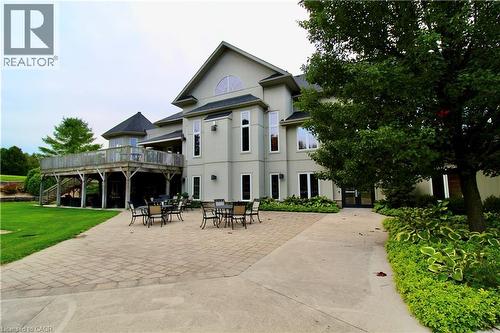 Stucco exterior with multiple windows, elevated wooden deck, extensive paver patio, and mature landscaping - 40 Stornoway Crescent, Huron East, ON 