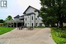 Stucco exterior with multiple windows, elevated wooden deck, extensive paver patio, and mature landscaping - 40 Stornoway Crescent, Huron East, ON 